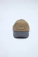 Gorra clásica con diseño en bloque de color, cuerpo en tono beige y visera en verde. Cuenta con bordado frontal con la palabra 'UNIFORM'.