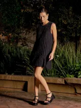 Vestido corto de punto sin mangas, con diseño de rayas verticales en tonos azul marino y negro con hilos de lurex. Presenta un corte recto con un volado en el ruedo que aporta movimiento.