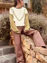 Sweater color crudo con mangas largas color verde oliva. Presenta cuello redondo y detalle de bordado con pompones en forma de V en el frente.