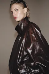 Chaqueta de corte amplio estilo biker en tejido efecto piel de color verde oscuro, con cuello alto envolvente, cierre frontal asimétrico de cremallera metálica, bolsillos ocultos en costura y forro interior.