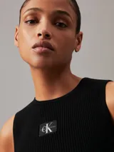 Musculosa Calvin Klein de corte slim, confeccionada en tejido de punto de canalé suave y elástico. Presenta cuello redondo, diseño sin mangas y una insignia con el monograma de la marca en el pecho.