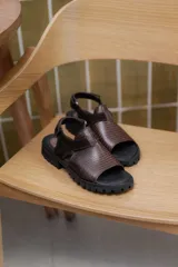 Sandalias de cuero con textura grabada, diseño de punta abierta y talón descubierto con tira ajustable. Poseen una suela de plataforma dentada en tono tierra.