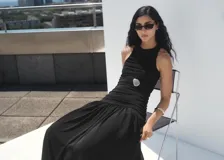 Vestido midi negro sin mangas, con cuello redondo y diseño ajustado en el torso mediante fruncidos laterales, que se abre en una falda evasé fluida.