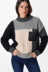 Sweater de punto con diseño patchwork en bloques de color negro, gris y crudo. Presenta cuello redondo acanalado, mangas largas con puños elásticos y un bolsillo frontal tipo parche con textura trenzada.