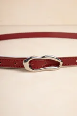 Cinturón fino color rojo de símil cuero con hebilla metálica irregular plateada.