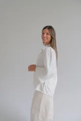 Camisa blanca de corte holgado con cuello clásico, cierre frontal de botones y mangas tres cuartos con sutil detalle bordado en los puños.