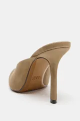 Zapato tipo mule con tacón alto fino y acabado en punta, confeccionado en material con textura gamuzada.