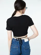 Top blanco de manga corta con cuello redondo y un diseño fruncido en el busto que deja expuesto el abdomen, atado con tiras cruzadas alrededor de la cintura.