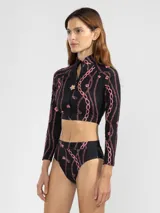 Crop top de bikini negro con estampado de cadenas rosas, cierre frontal con cremallera y detalle de flor en el cuello.