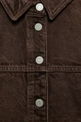 Cazadora de denim en color azul oscuro con costuras en contraste, cuello solapa, manga larga y cierre frontal con botones metálicos. Presenta dos bolsillos de plastrón en el delantero.