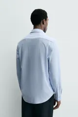 Camisa de manga larga, color celeste con finas rayas verticales blancas, cuello italiano y cierre frontal de botones.