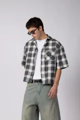 Camisa de manga corta de popelina cuadrillé en tonos marrón, blanco y gris, con diseño boxy fit, cuello camisero, cierre frontal de botones, bolsillo en el pecho con detalle bordado y dobladillo recto.