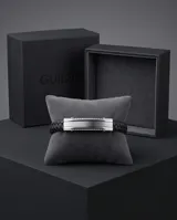 Pulsera masculina de diseño moderno, compuesta por una banda central de acero inoxidable pulido y laterales de cuero trenzado negro. Cuenta con un cierre de seguridad integrado.