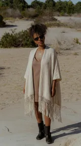 Ruana color crudo con tejido artesanal, corte amplio y flecos largos en el ruedo.