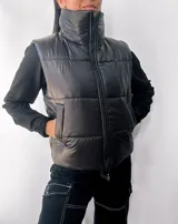 Chaleco puffer negro con cuello alto y cierre frontal con cremallera. Tiene bolsillos laterales y diseño acolchado.