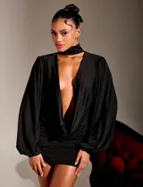 Vestido corto negro con escote profundo, cuello tipo choker integrado y mangas largas con volumen. Presenta un diseño drapeado en la cintura y falda ajustada al cuerpo.