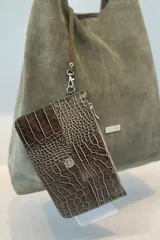Bolso tipo tote de gran capacidad, confeccionado artesanalmente en cuero vacuno color marrón. Presenta un diseño minimalista con costura central vertical, fuelle lateral ajustable con cierre y placa metálica con logo en la parte inferior.