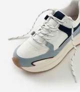 Championes estilo jogging con diseño de recortes contrastantes en tonos blanco, azul y gris. Presenta una parte superior de mesh respirable con sobreposiciones de poliuretano, forro suave y suela robusta de color crema con base marrón.