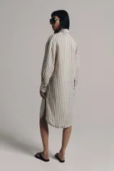 Vestido midi estilo camisero de Zara Woman Collection, confeccionado en lino, con estampado de rayas verticales azules sobre fondo beige. Cuenta con cuello solapa, escote en V con botonadura parcial, manga larga con puños abotonados, un bolsillo de plastrón en el pecho y bajo redondeado.