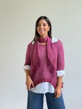 Sweater de punto color magenta con diseño asimétrico, cuello redondo y detalle de encaje bordado en el frente. Incluye una bufanda del mismo tejido y color, y se presenta superpuesto sobre una camisa blanca de algodón.