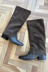 Bota de caña alta confeccionada en una combinación de cuero vacuno liso en la base y gamuza en la caña. Presenta un diseño de caña holgada, puntera redondeada y taco cuadrado bajo.