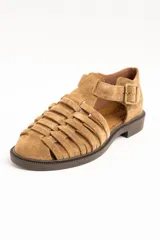 Sandalias cangrejeras de gamuza color visón, con diseño de tiras entrelazadas, tira ajustable con hebilla metálica en el tobillo y suela plana de goma marrón.