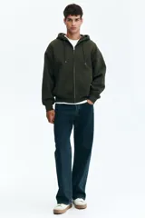 Campera con capucha y cierre frontal, color verde militar oscuro, de tejido pesado con interior cepillado suave. Presenta hombros caídos, cordón ajustable en la capucha y bolsillos canguro delanteros.