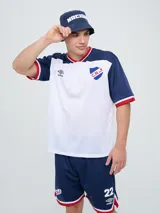 Remera de fútbol Umbro del Club Nacional de Football, de diseño tricolor con cuerpo azul marino, mangas y canesú rojos, y cuello en V con detalles en blanco y azul. Incluye el logo de Umbro en el pecho derecho y el escudo del club en el izquierdo.
