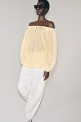 Blusa de lino color blanco, con escote recto ajustable mediante cordón y hombros descubiertos. Cuenta con manga larga abullonada terminada en elástico.
