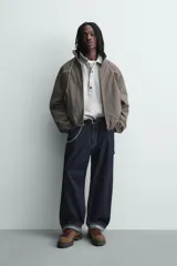 Cazadora de corte boxy fit confeccionada en tejido técnico. Presenta un diseño a rayas verticales, cuello subido, cierre frontal de cremallera y mangas largas con puños elásticos. Incluye bolsillos laterales con cremallera oculta y detalles de paneles en contraste.