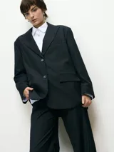 Blazer de corte sastre en color negro, con cierre frontal de dos botones, solapas clásicas y bolsillos laterales con solapa.