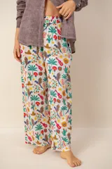 Pantalón ancho color blanco con estampado colorido de loros, cactus, sombreros mexicanos, guitarras y flores, de corte holgado y cintura elástica fruncida.