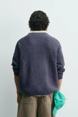 Jersey de hombre de corte relajado, color azul oscuro o morado apagado, con textura rizada (bouclé) y cuello redondo.