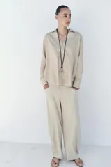 Blusa amplia confeccionada en mezcla de viscosa y lino, color beige, con cuello solapa, escote en V y manga larga.