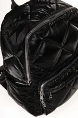 Mochila plateada capitoneada tipo puffer con compartimentos laterales, dos bolsillos externos con cierre y tres bolsillos adicionales en su interior. Cuenta con un asa fija en la parte superior y dos regulables en la espalda.