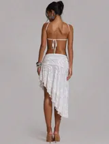 Vestido midi asimétrico blanco con escote halter cruzado, recortes profundos y espalda descubierta. Cuenta con falda de caída irregular, frunce en la cintura y aplique metálico central.