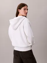 Buzo Calvin Klein de color blanco, con capucha ajustable mediante cordones, cierre frontal con cremallera y bolsillos tipo canguro. Presenta mangas largas y logo bordado en el pecho.