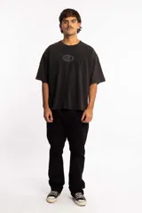 Remera de corte boxy fit, color negro con efecto lavado, de manga corta y cuello redondo. Presenta un logo bordado en el centro del pecho dentro de un óvalo.