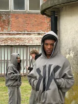 Campera con capucha gris oscura, cierre frontal y diseño oversize con doble capucha, incluyendo balaclava integrada. Presenta gran estampa contrastante en el frente.