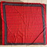 Pañuelo cuadrado de seda color rojo con estampado de lunares negros y bordes decorados con guardas ornamentales.