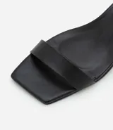 Sandalias negras de cuero sintético, con punta cuadrada, tira fina sobre los dedos, pulsera con hebilla al tobillo y tacón geométrico bajo.