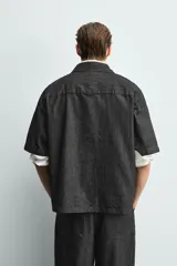 Camisa de manga corta con cuello solapa y cierre frontal de botones. Confeccionada en tejido denim de algodón, de corte relajado y aberturas laterales en el bajo.