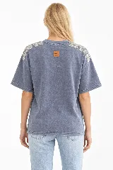 Remera oversize de algodón con acabado stonewash, color gris azulado, manga corta y cuello redondo. Cuenta con apliques bordados a mano en forma de hojas con canutillos plateados sobre los hombros.