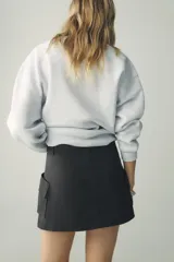 Falda pantalón negra de tiro medio, confeccionada en algodón, con pliegue frontal y maxi bolsillos cargo con solapa y cremallera en ambos lados.
