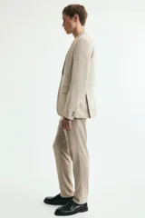 Pantalón de traje beige de corte slim fit, con cierre frontal con cremallera y corchete oculto, trabillas para cinturón, bolsillos laterales y bolsillos traseros ribeteados. Cuenta con raya marcada al frente.
