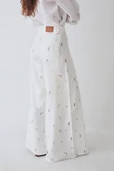 Pantalon de corte wide leg y tiro alto, confeccionado en tela con estampado deportivo que incluye pelotas de futbol y raquetas de tenis en tonos verde, rosa y beige.