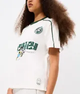 Remera boxy de algodón color blanco, con cuello redondo y ribete verde oscuro, manga corta con líneas decorativas en los hombros, y estampado frontal deportivo de Mickey Mouse con tipografía.