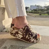 Sandalias de plataforma con estampa animal print de vaca en color marrón y blanco, confeccionadas en cuero con pelo natural. Cuentan con suela de micro y taco de 6 centímetros.