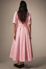 Vestido midi de estilo camisero color rosado, con cuello solapa, manga corta y cierre frontal con botones. Presenta bolsillos de plastrón con solapa en el pecho, bolsillos laterales ocultos y un cinturón del mismo tejido para ajustar en la cintura.