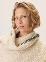 Triángulo de lana color beige con maxi flecos, diseñado por Margara Shaw en colaboración con Manos del Uruguay. Confeccionado con una mezcla de lana merino, mohair, viscosa, algodón y otras fibras, incluyendo lurex y un hilado teñido a mano con lentejuelas.